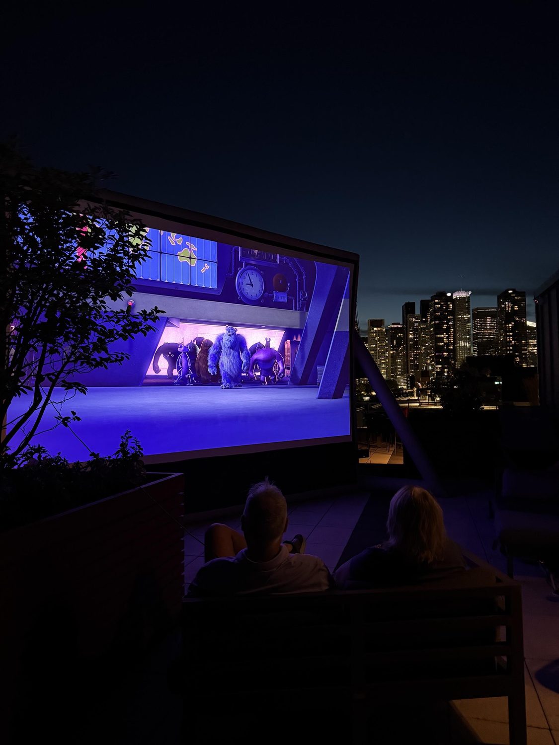 Outdoor movie night on a rooftop with the city skyline behind the screen