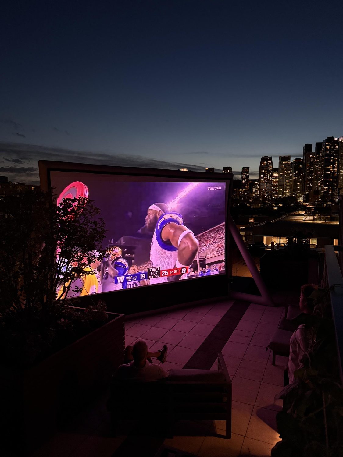 Rooftop sports watch party on a 200-inch outdoor screen with the Montreal skyline at dusk