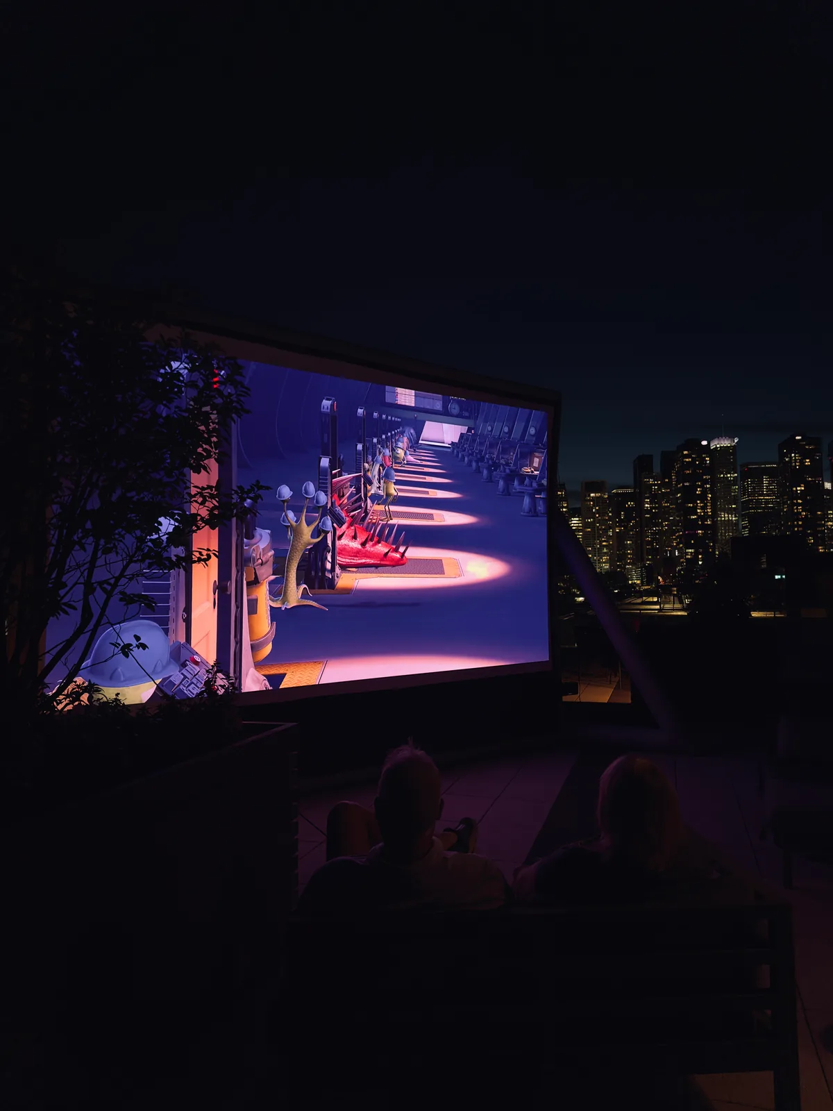 Guests watching a rooftop movie with the city skyline behind the screen